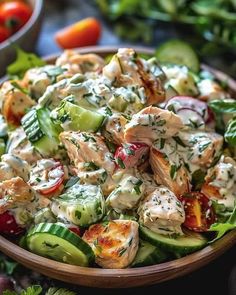 a wooden bowl filled with chicken salad next to tomatoes, cucumbers and lettuce