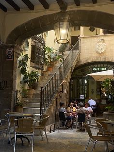 several people sitting at tables under an archway in a restaurant with stairs leading up to the second floor