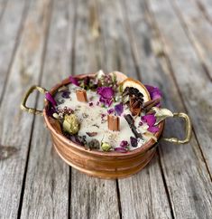 a copper bowl filled with flowers on top of a wooden table next to an orange slice