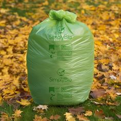 a large green bag sitting on top of a field covered in yellow and orange leaves