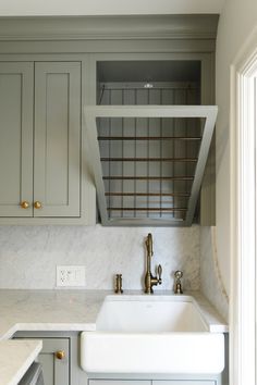 a kitchen with marble counter tops and gray cabinets, including a white farmhouse style sink