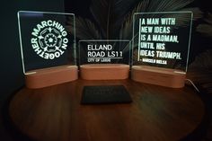 three illuminated signs sitting on top of a wooden table next to a black book and palm tree