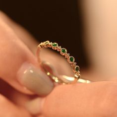 a woman's hand holding a gold ring with green stones