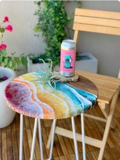 a wooden table topped with a colorful painted stool next to a potted plant and bottle