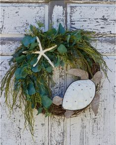 a wreath with starfishs and greenery hangs on a door handle, decorated with seashells