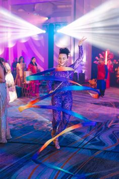 a woman is dancing with colorful streamers in her hand and lights on behind her