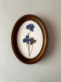 blue flowers in a wooden frame mounted on the wall by a white wall behind it