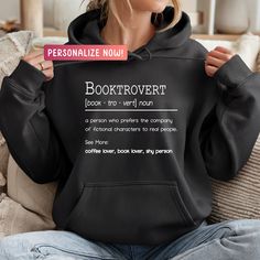 a woman sitting on a couch holding up a black hoodie that says booktrover