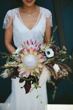 a woman in a white dress holding a large bouquet with flowers on it's side