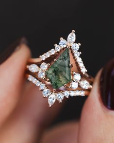 a woman's hand holding a ring with a green stone and diamonds on it