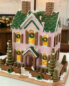 a pink gingerbread house decorated with icing and christmas wreaths on the roof