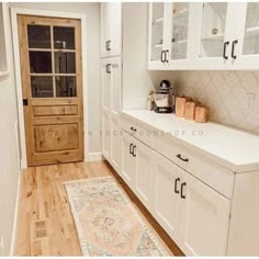 a kitchen with white cabinets and wood floors, an area rug in front of the door