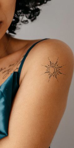 a woman with a sun tattoo on her left arm and shoulder is looking at the camera