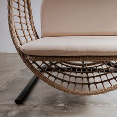 a wicker chair with cushion and black metal legs on concrete floor next to white wall