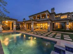 an outdoor swimming pool in front of a large house at night with the lights on