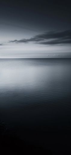 a lone boat floating on top of a large body of water under a cloudy sky