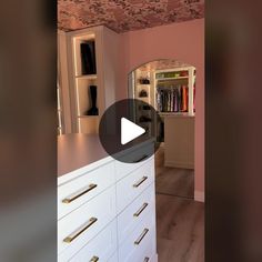 a walk in closet with white drawers and gold handles on the doors, along with a pink wallpapered ceiling