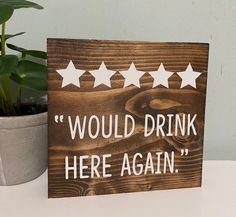 a wooden sign that says would drink here again next to a potted plant on a table