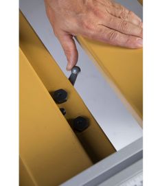 a hand is reaching for something on the side of a yellow and gray cabinet with black knobs