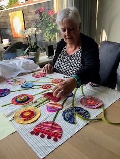 an older woman sitting at a table working on some crafting pieces with scissors and thread