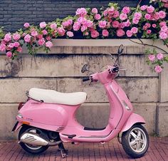 a pink scooter parked next to a wall with flowers