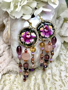 "DUSTY ROSE TRAILS  A beautiful and dramatic handmade pair of OOAK  earrings, featuring a cameo embellished with hand painted flowers, and edged with vintage rhinestones. The cameo is made from hand shaped and hammered brass wire, filled with resin. Trails of vintage glass beads, freshwater pearls and Amethyst briolettes dangle below the cameos.      * Lightweight     * Resin     * Entirely hand modelled, no moulds used.     * Leverback earwires     * Amethyst briolettes     * Czech glass beads Bohemian Jeweled Purple Jewelry, Bohemian Jeweled Beaded Dangle Earrings, Bohemian Style Jeweled Beaded Dangle Earrings, Bohemian Jeweled Dangle Beaded Earrings, Bohemian Jeweled Beaded Earrings For Gifts, Bohemian Jeweled Chandelier Earrings As Gift, Hammered Brass, Hand Model, Hand Painted Flowers