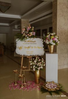 a sign that has flowers on it in front of some gold vases with pink and white flowers