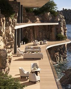 an outdoor deck with chairs and tables next to the ocean on a rocky cliff side