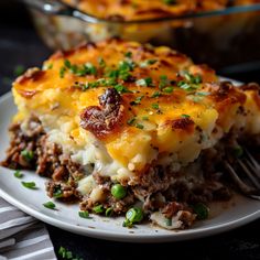 a white plate topped with lasagna covered in cheese and green onions next to a casserole dish