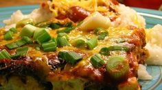 a blue plate topped with an enchilada covered in cheese and green onions