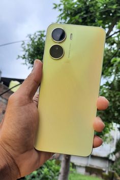 a person holding up a yellow cell phone in their hand with the camera on it