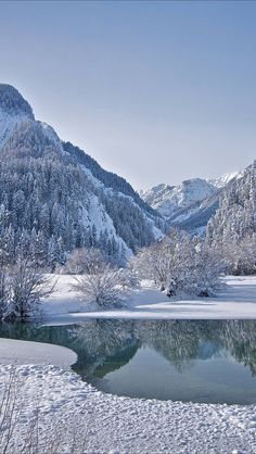 a lake surrounded by snow covered mountains in the middle of winter with trees on either side