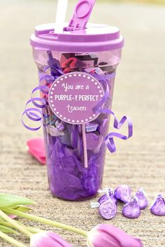 a purple cup filled with lots of candies next to tulips and flowers