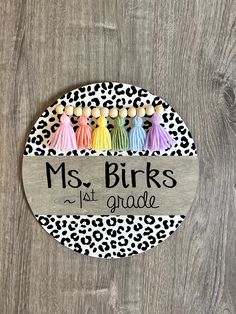 a wooden sign that says, ms birks 1st grade with colorful tassels on it