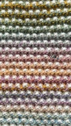 a close up view of a multicolored crochet knitted blanket with a small object in the middle