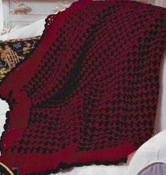 a red blanket sitting on top of a bed next to a pillow and a clock