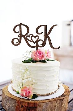 a white cake with pink flowers and an arrow on top is sitting on a wooden table