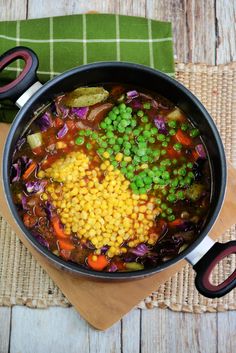 a pot filled with vegetables and peas on top of a wooden cutting board next to scissors