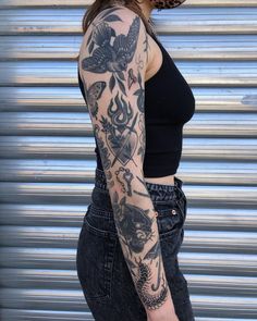 a woman with a tattoo on her arm and leg is standing in front of a garage door