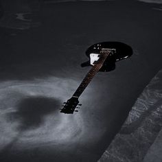 a black and white photo of an electric guitar in the dark with water around it