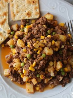 a white plate topped with meat and veggies next to crackers