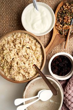 bowls of cereal, yogurt and raisins with spoons on the side