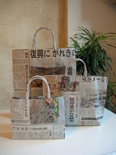 three newspaper bags sitting next to each other on a white table with a plant in the background