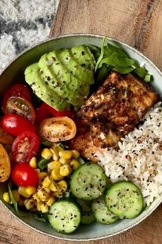 a bowl filled with rice, cucumbers, tomatoes and other vegetables on top of a wooden table