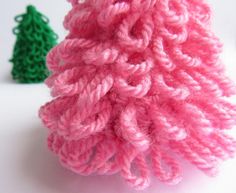 a pink knitted christmas tree next to a green crochet ornament