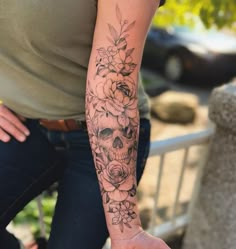 a woman with a skull and flowers tattoo on her arm, holding onto a hand