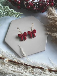 two red bows are attached to the back of small earrings on a piece of white paper