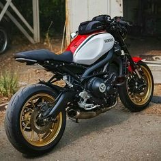 a red, white and black motorcycle parked in front of a building with gold rims