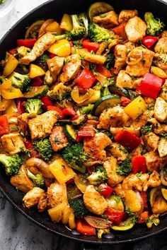 a skillet filled with chicken, broccoli, peppers and other veggies