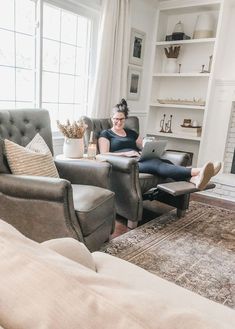 a woman sitting in a chair with her feet up on the couch while using a laptop